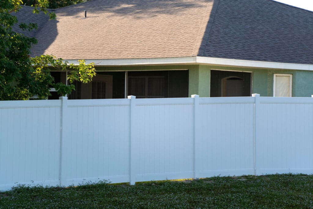 White vinyl picket fence on green lawn surrounding property grounds for backyard protection.